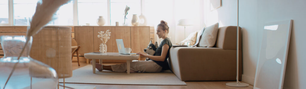 Image of a woman sitting on the ground in her living room with her dog while surfing the internet and listening to music.
