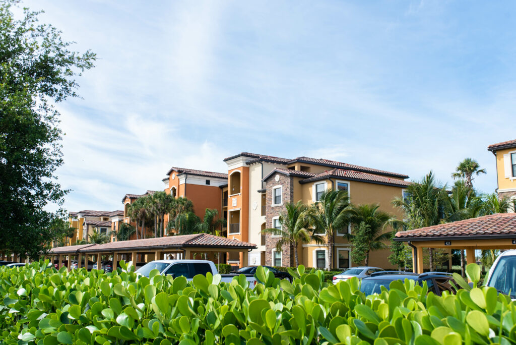 Several large multi-unit buildings with a view of the parking lot and nearby trees.