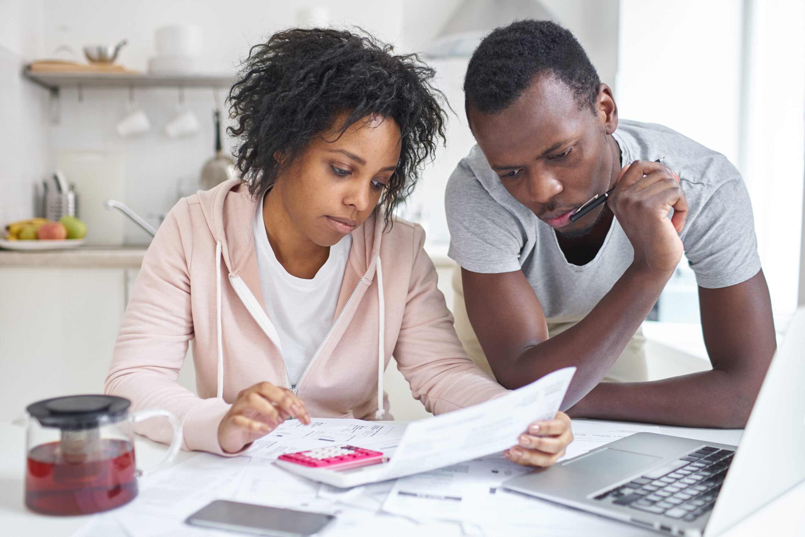 Man and woman looking at a financial document and calculating their budget at the kitchen table.
