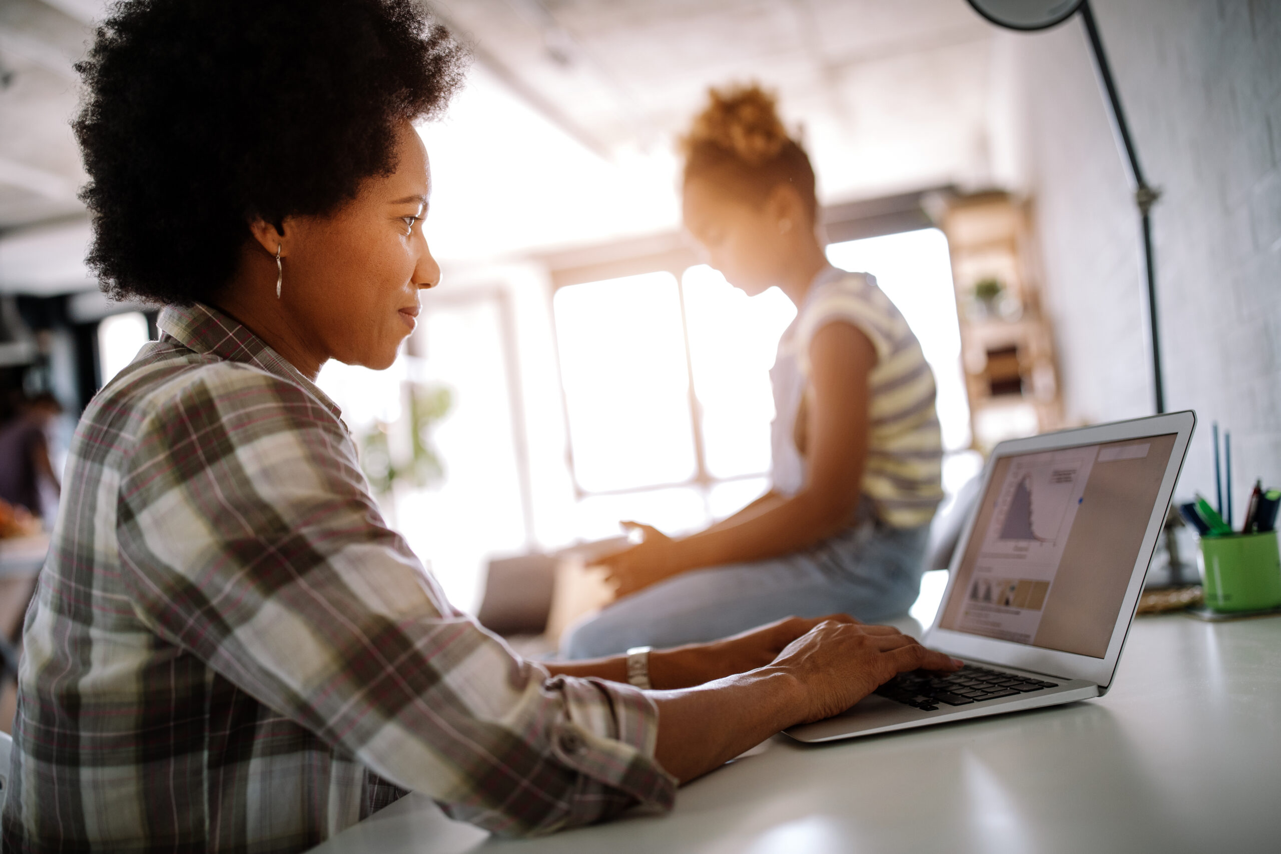 Woman working on research while a girl sits nearby.