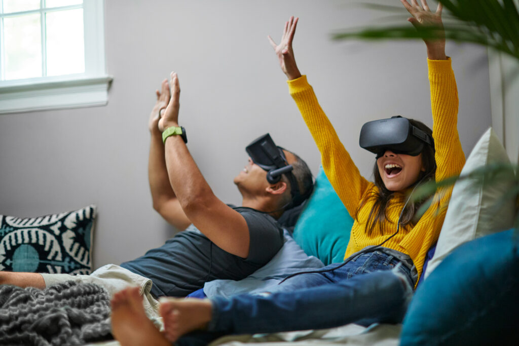 A father and daughter sitting on the couch with virtual reality headgear on.