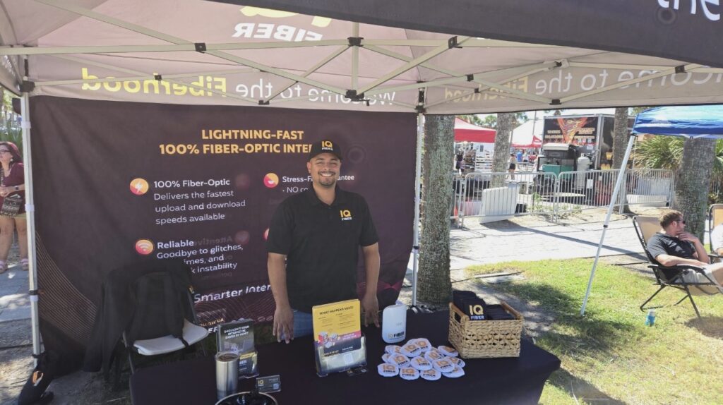 IQ Fiber employee standing in front of a lightning fast fiber optic internet sign at an event.