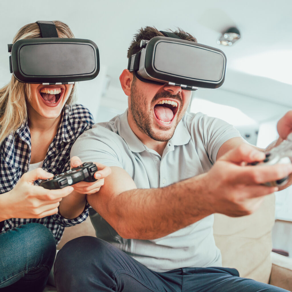 Two friends sitting on the couch playing a video game with virtual reality headgear on their heads.