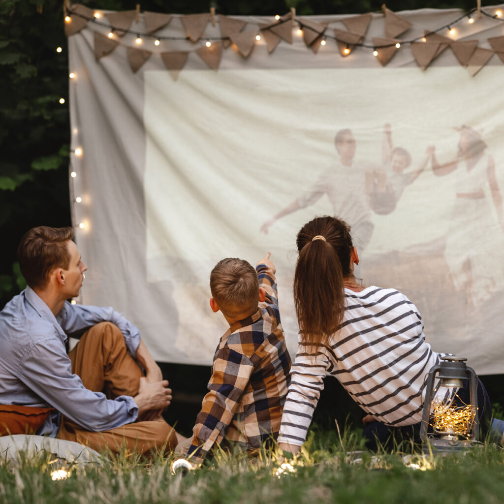 A family sitting outside watching a home video on a projector screen.